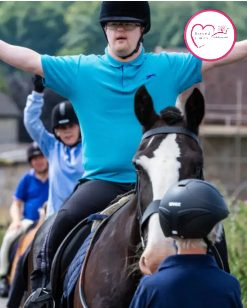 A participant in a riding helmet on horseback, arms raised in celebration