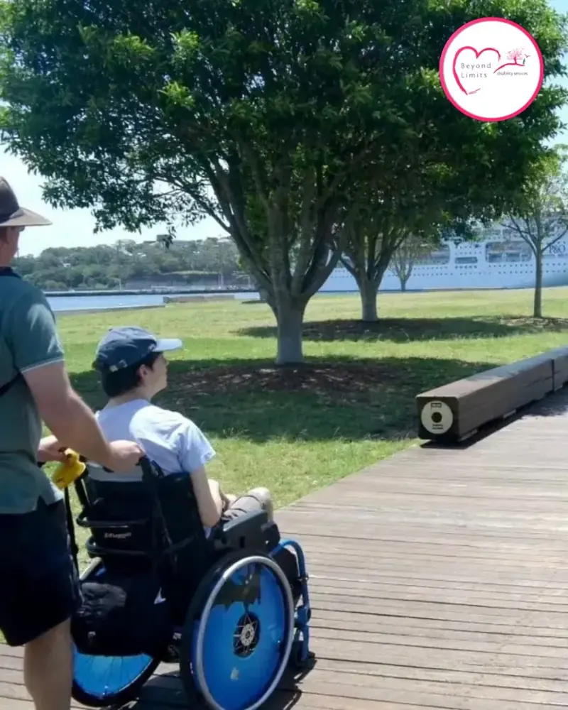 A support worker pushing a participant in a wheelchair along a waterfront path